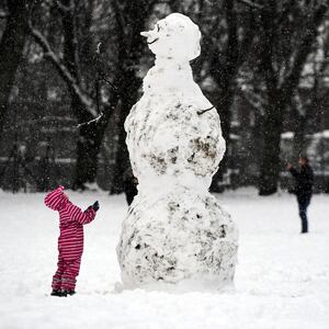 A child looks at a giant snowman as they stand in a snow-covered Victoria Park in Glasgow on February 9, 2021.
