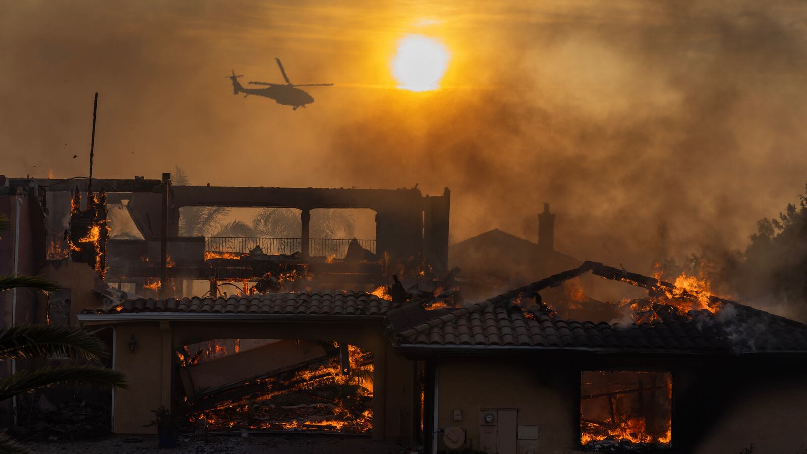 A firefighting helicopter flies near as a home burns.