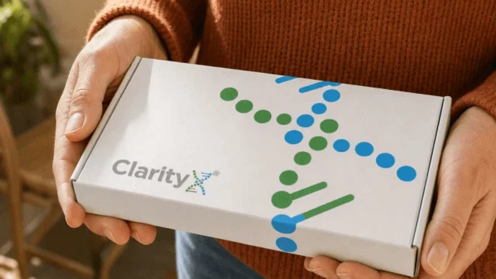 Person holding the ClarityX at-home DNA test kit box, featuring a colorful DNA helix graphic.