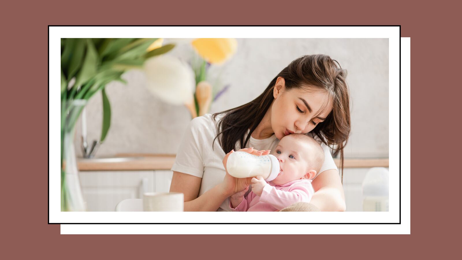 A mother lovingly feeds her baby with a bottle, surrounded by soft natural light and a vase of flowers in the background. The baby is dressed in a pink outfit and looks content, while the mother gently holds the bottle and gazes at her child with affection.
