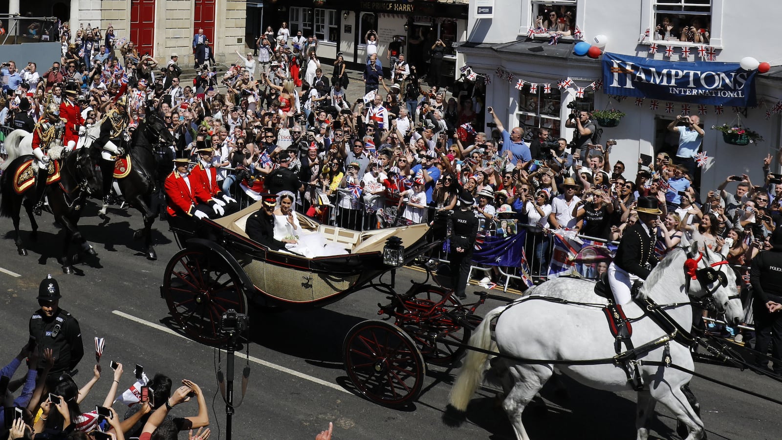 Prince Harry, Duke of Sussex and his wife Meghan, Duchess of Sussex wave from the Ascot Landau Carriage during their carriage procession on the High Street in Windsor, on May 19, 2018