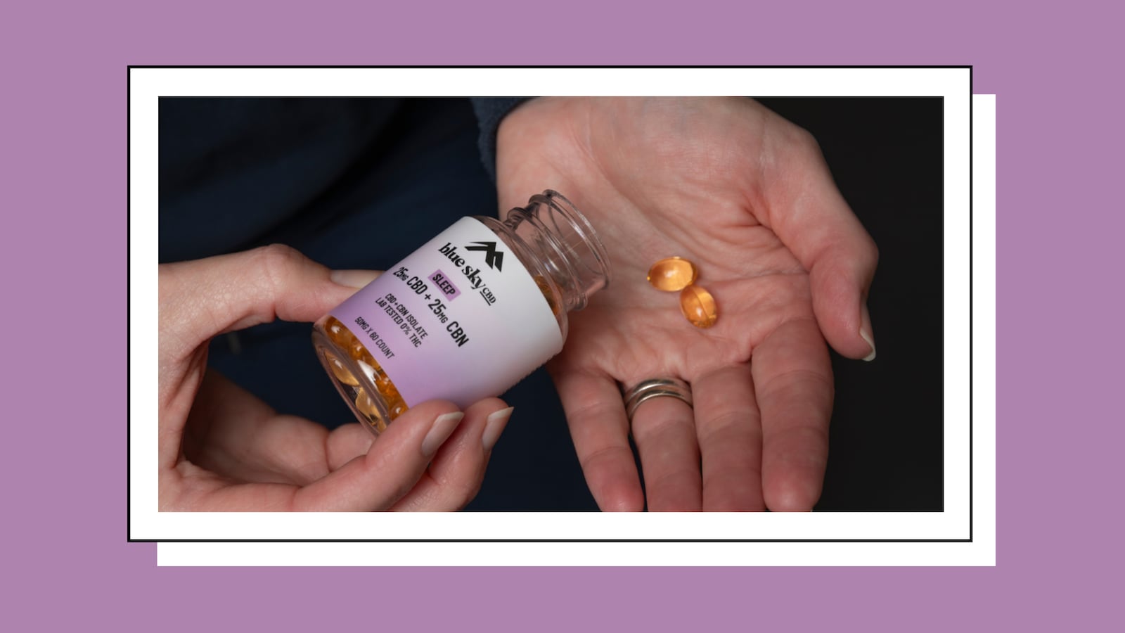 Close-up of two hands: one pouring softgel capsules from a Blue Sky CBD Sleep bottle (25mg CBD + 25mg CBN) into an open palm holding two golden softgels, against a dark background with a lavender border.