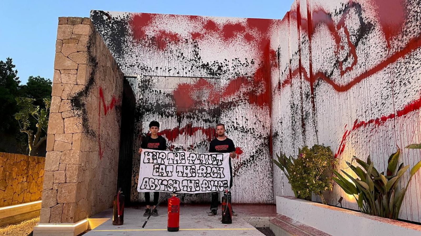 Two climate activists standing in front of Lionel Messi's house after vandalizing it.