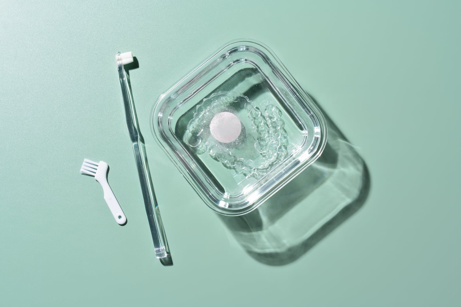 Cleaning Invisible Braces by Using Brushes With Effervescent Tablet on Green Background Directly Above View.