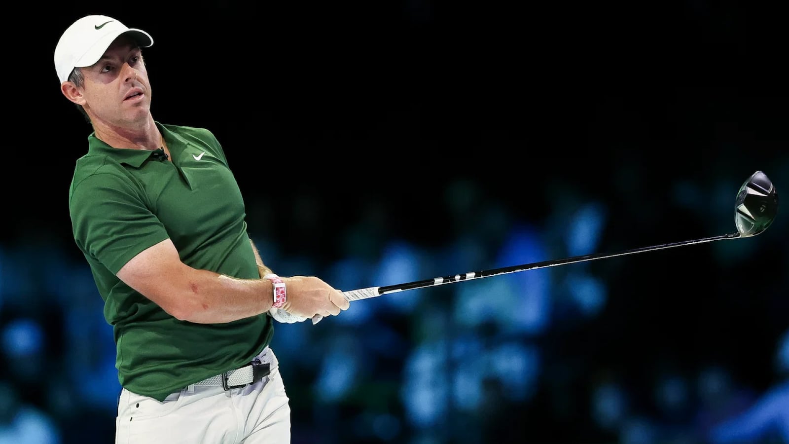 Rory McIlroy mid-swing with a driver, wearing a red and white WHOOP wearable on his left wrist, dressed in a green polo and white cap.