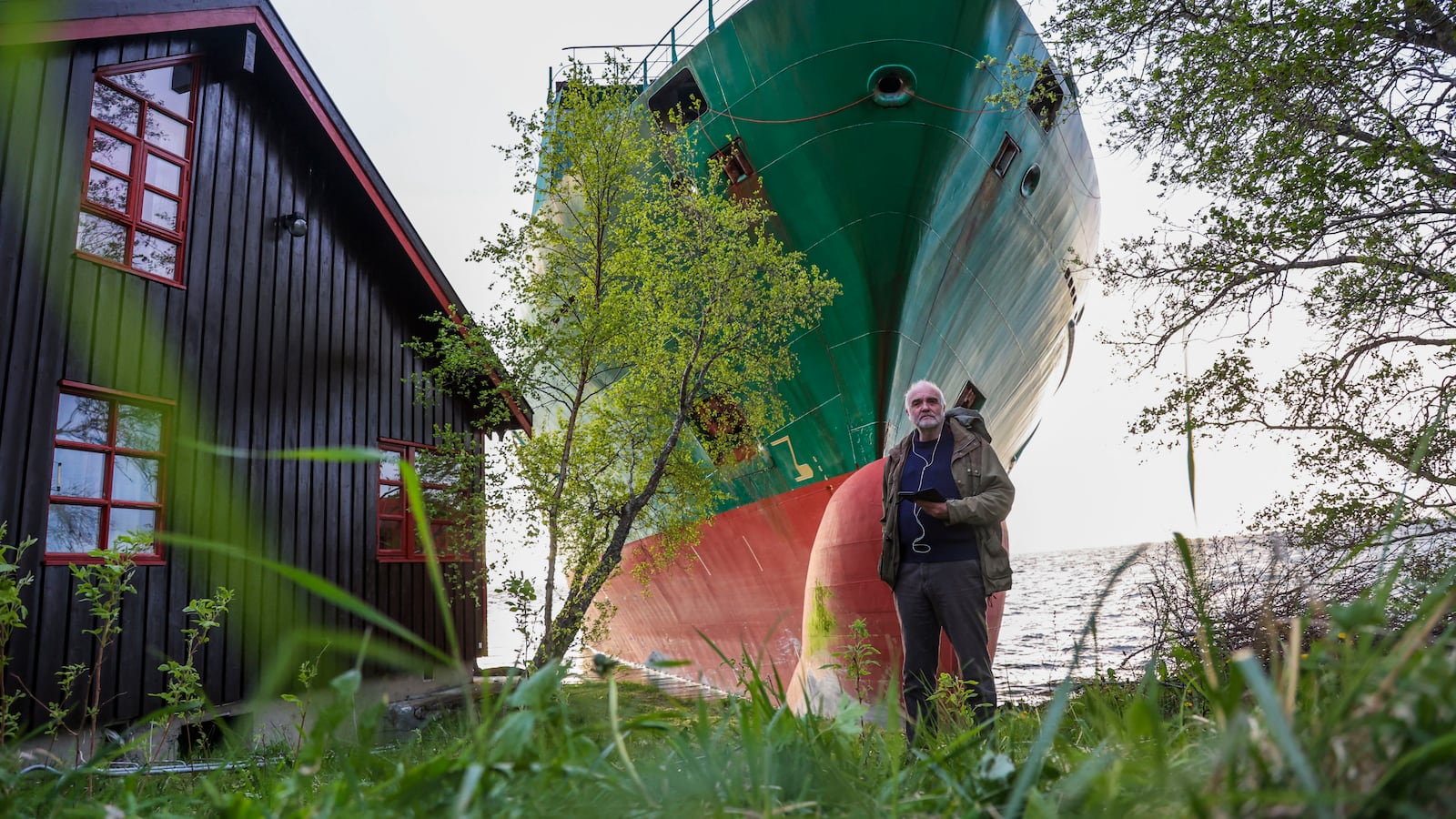 Johan Helberg's pose next to his house and a 135-meter-long container ship by the shore in the Trondheimsfjord outside Byneset by Trondheim, Norway, on May 22, 2025, after the ship ran aground almost hitting his house. (Photo by Jan Langhaug / NTB / AFP) / Norway OUT (Photo by JAN LANGHAUG/NTB/AFP via Getty Images)
