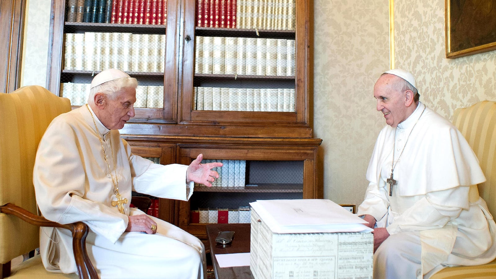 Pope Francis and Pope Benedict XVI meet in 2013 and Castel Gandolfo, with a big white box sitting between them.