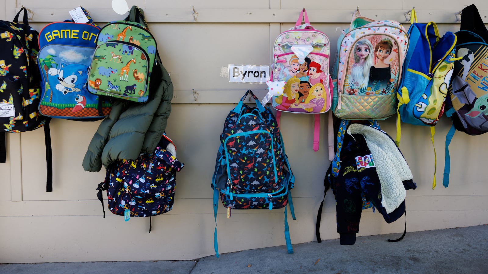 Backpacks hang on the wall outside a classroom