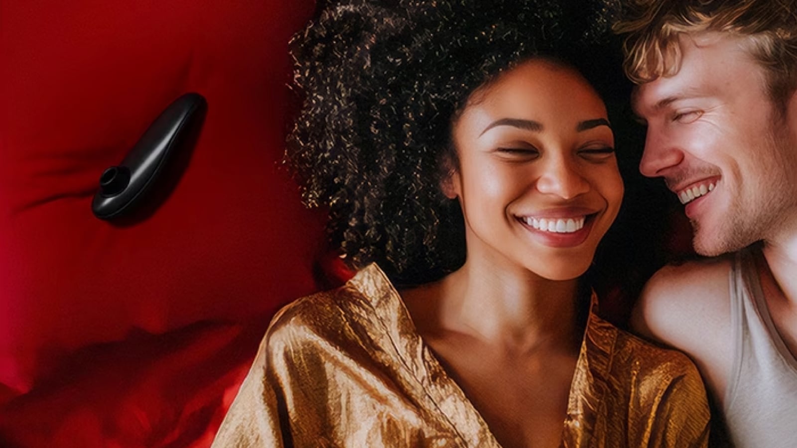 A couple lying on a bed. They are both smiling and to the right of them is a clitoral stimulator.