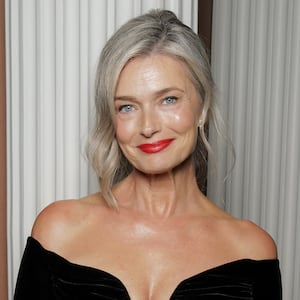 Model Paulina Porizkova wears a black long-sleeve, off-the-shoulder gown. Her gray hair is pulled back and she's wearing red lipstick.