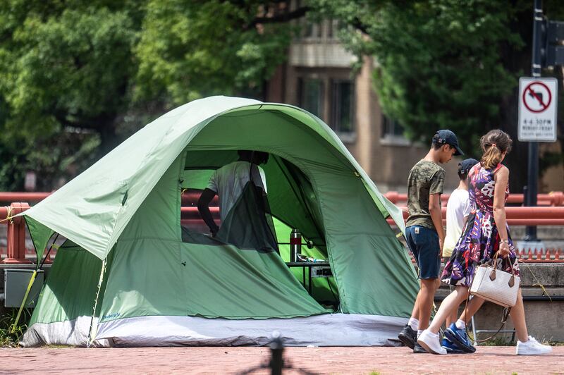 People walk past tents at a homeless encampment in Washington, DC, on August 13, 2025 as President Donald Trump vowed to crackdown on homelessness as part of his attempt to clean up the nation's capital and complains about crime and crumbling road medians.