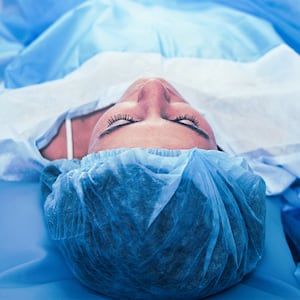 Young lady lying on the operation table with a surgical screen covering her body below the waist