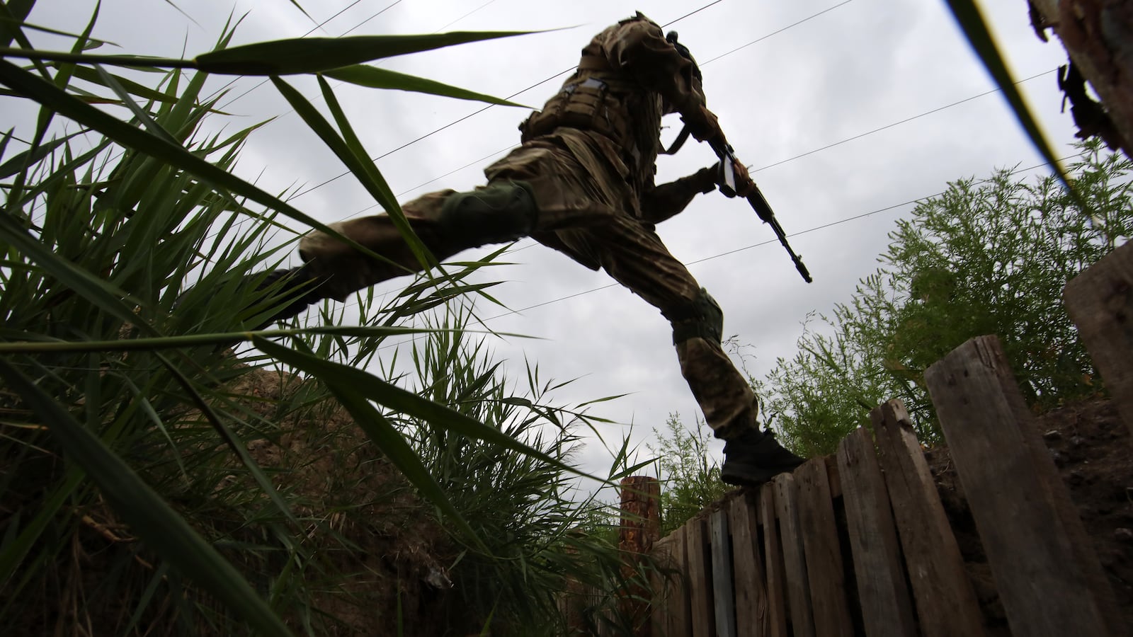 An armed National Guard serviceman jumps across a trench outside Kharkiv in Ukraine.