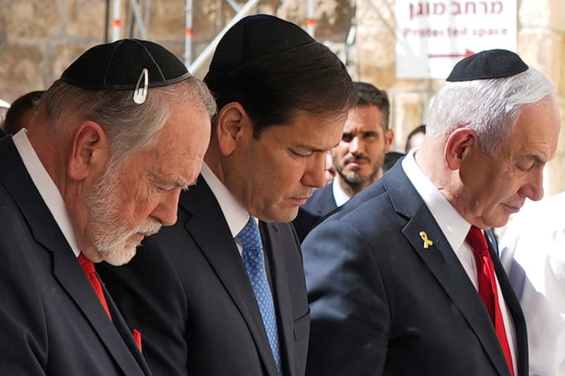 Three men wearing kippahs ow their heads in prayer at the Western Wall.