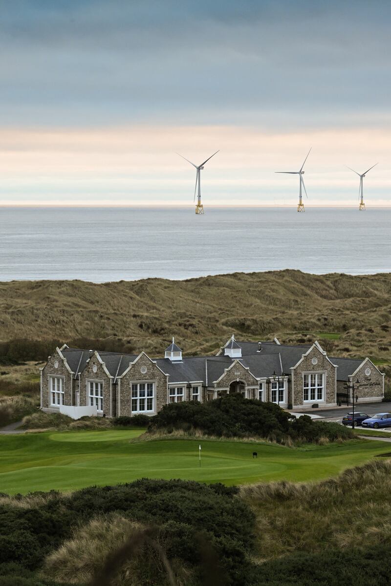 A club house at Trump International Golf Links in Balmedie, Scotland, with water and offshore wind turbines behind it.