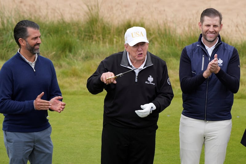 U.S. President Donald Trump holds scissors to cut the ribbon as he stands beside Donald Trump Jr. and Eric Trump during the opening ceremony for Trump International Golf Links near Aberdeen, Scotland, Britain July 29, 2025.  Alastair Grant/Pool via REUTERS