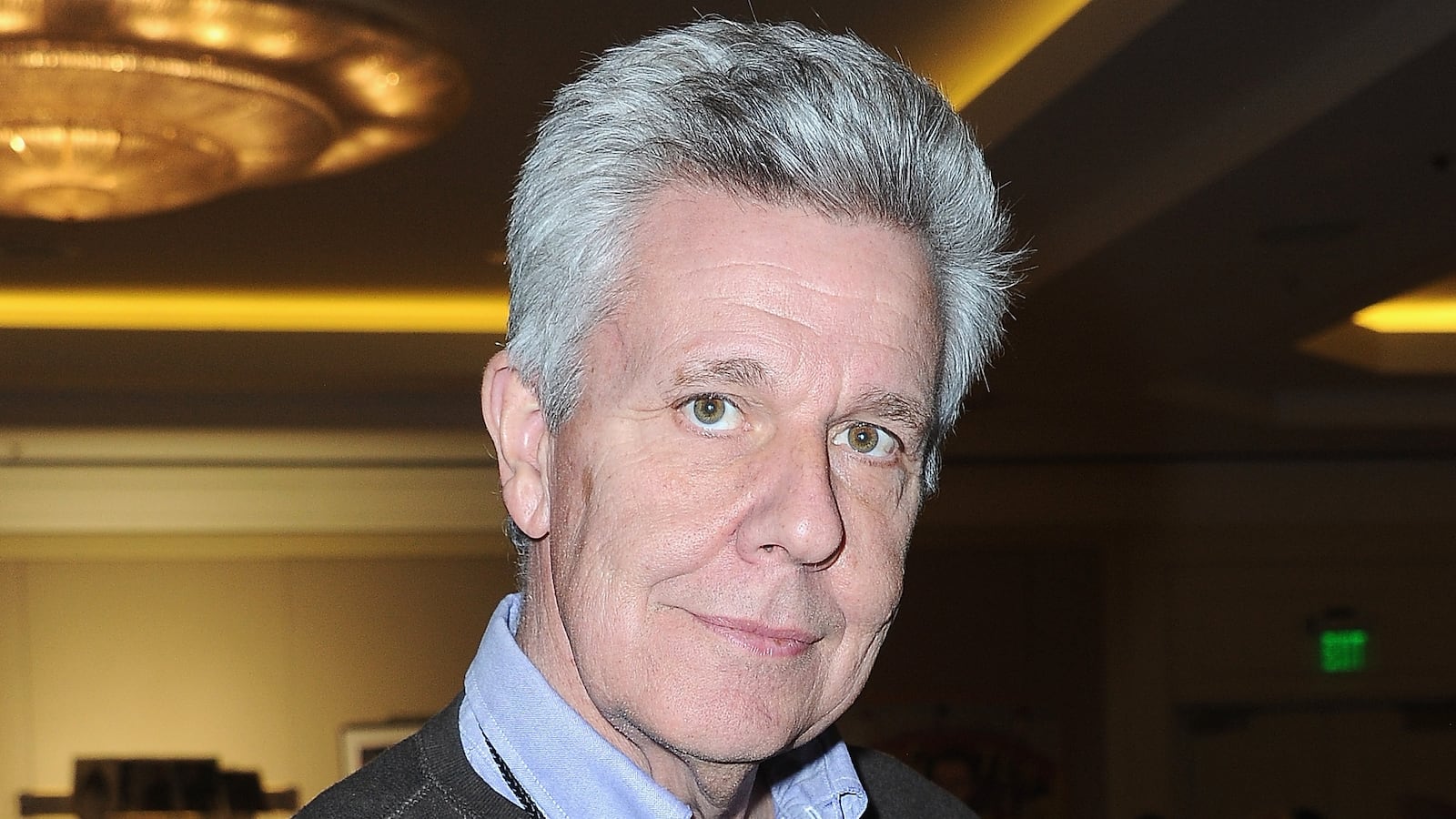 A grey-haired man holds an action figure of a man in a gimp costume.