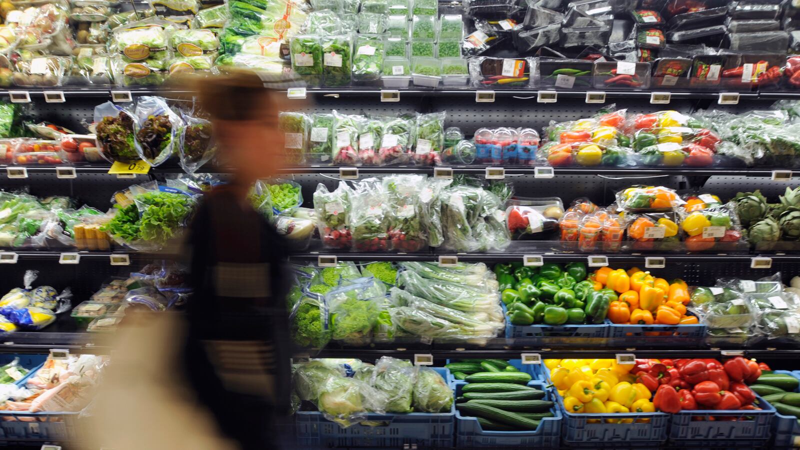 An individual walks past fresh fruits and vegetables at a grocery store.