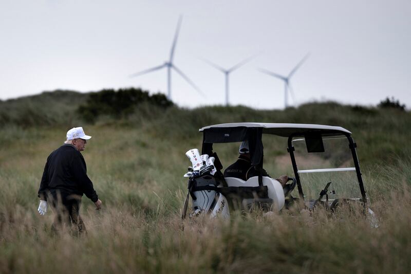 US President Donald Trump (L), backdropped by Turbines at the European Offshore Wind Deployment Centre, also known as the Aberdeen Bay Wind Farm, walks on the first fairway after playing off the first tee to officially open the Trump International Golf Links course in Balmedie, Aberdeenshire, north east Scotland on July 29, 2025. (Photo by Brendan Smialowski / AFP) (Photo by BRENDAN SMIALOWSKI/AFP via Getty Images)