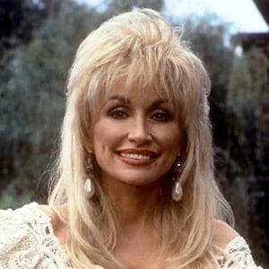 Dolly Parton poses with her guitar in front of Dollywood sign.
