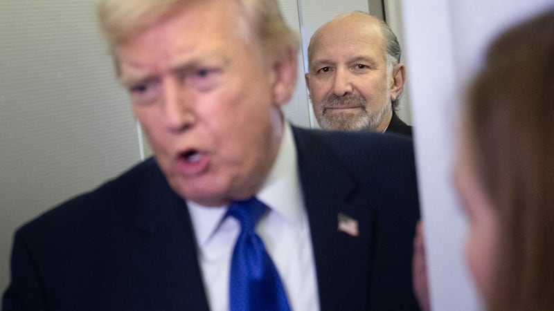 US Secretary of Commerce Howard Lutnick (rear) listens as US President Donald Trump speaks to reporters aboard Air Force One on his way to Palm Beach International Airport on February 6, 2026. The President is spending the weekend at his Mar-a-Lago residence. (Photo by Brendan Smialowski / AFP via Getty Images)