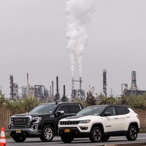 A photo of greenhouse gases being emitted from a pair of tall smokestacks in an industrial area.