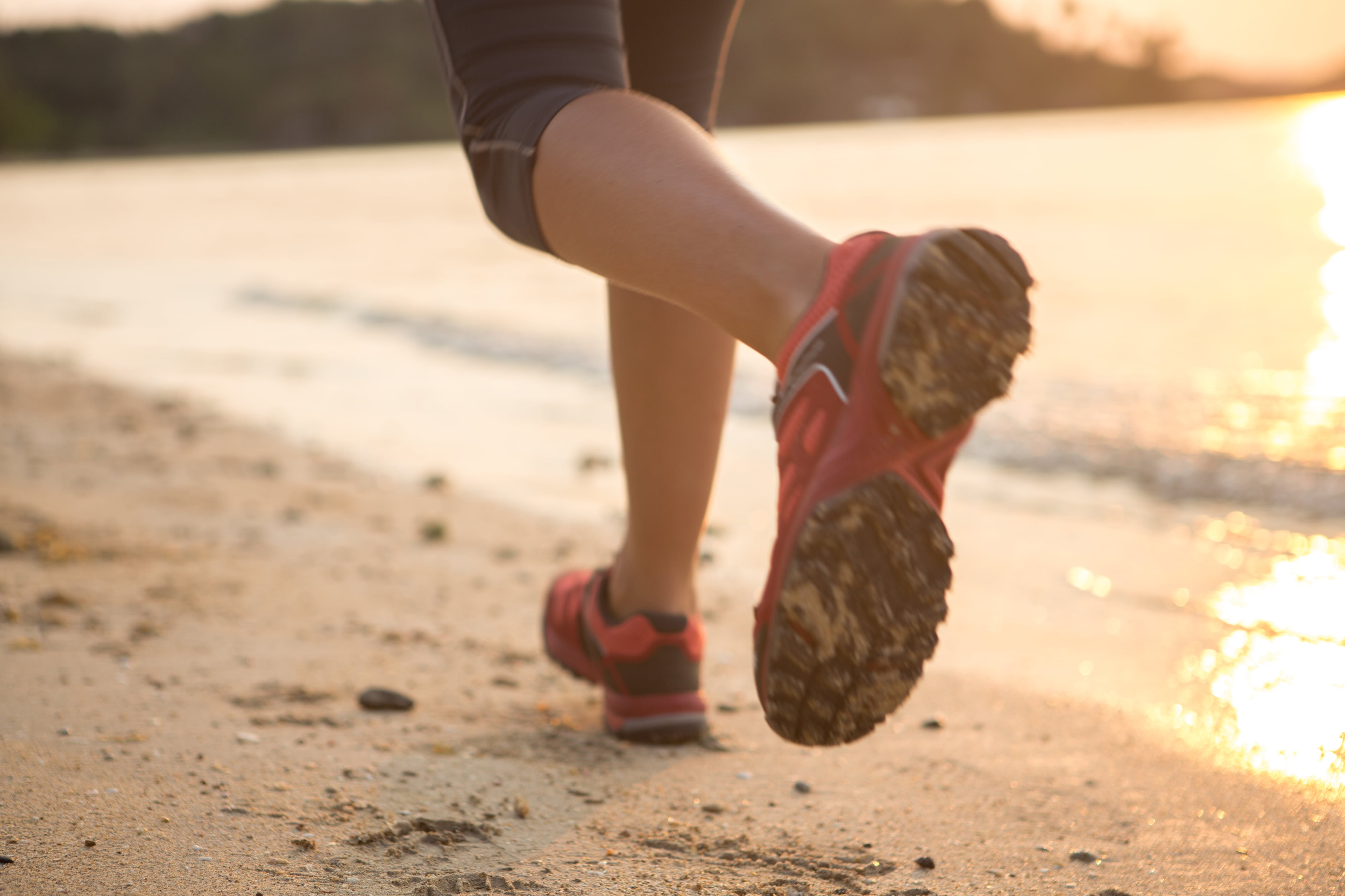 close-up of woman's sneakers as she runs on the beach at sunset