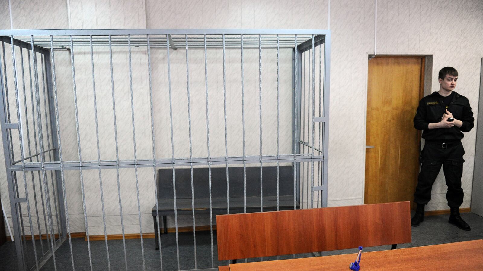 A security guard stands next to the empty defendant's cage in a Moscow court.