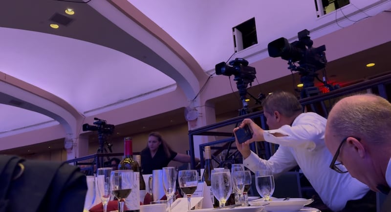 A man in a white hirt holds a phone in a large room