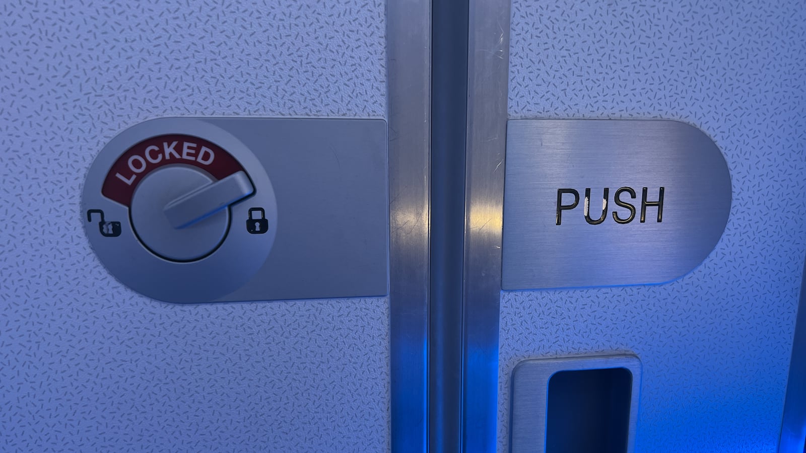 Door lock on interior door of airplane restroom on Airbus aircraft, with blue lighting.