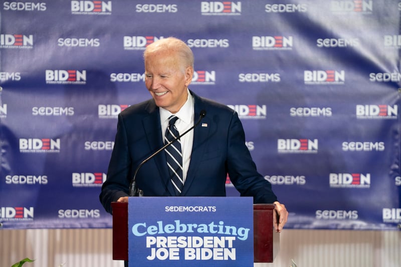 Former President Joe Biden laughing at a podium with a sign that reads: 'Celebrating President Joe Biden'