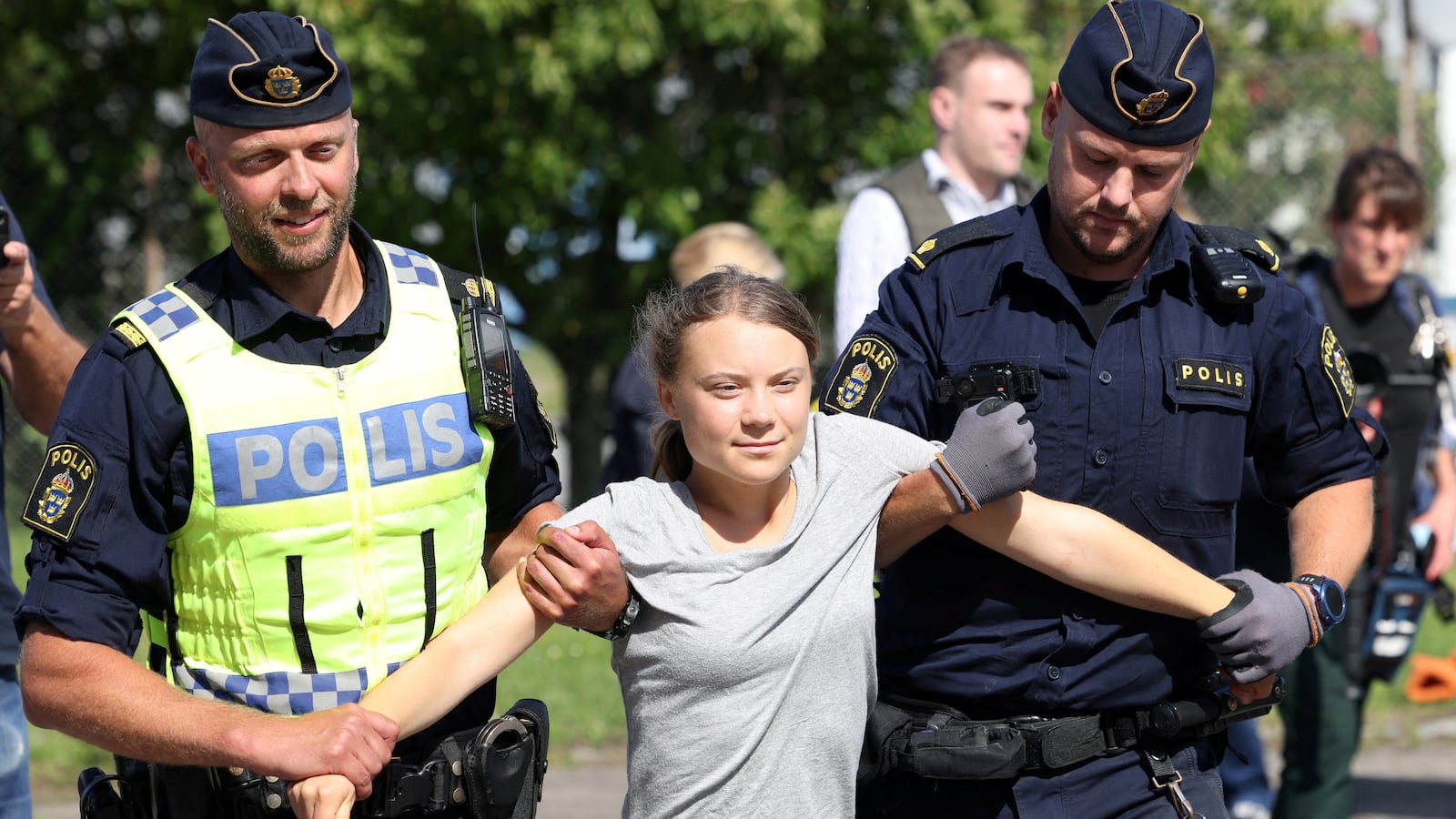 Greta Thunberg smirks as two Swedish cops remove her from a climate protest.