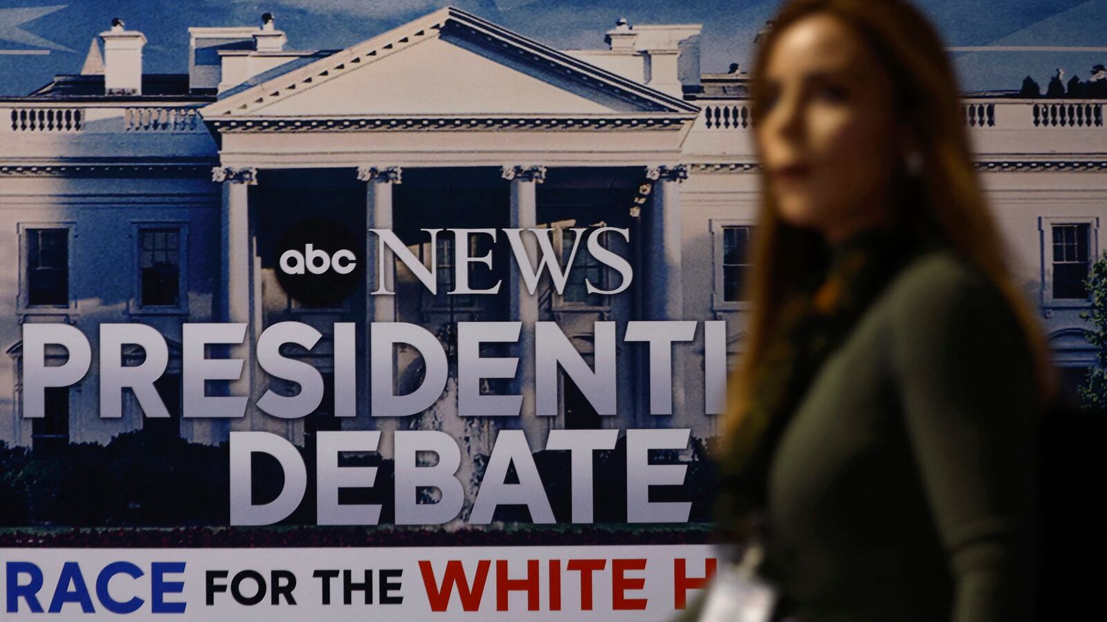 A person walks in front of a sign advertising the presidential debate.