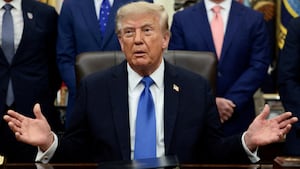 President Donald Trump speaks during a meeting in the Oval Office. He is surrounded by men in suits.