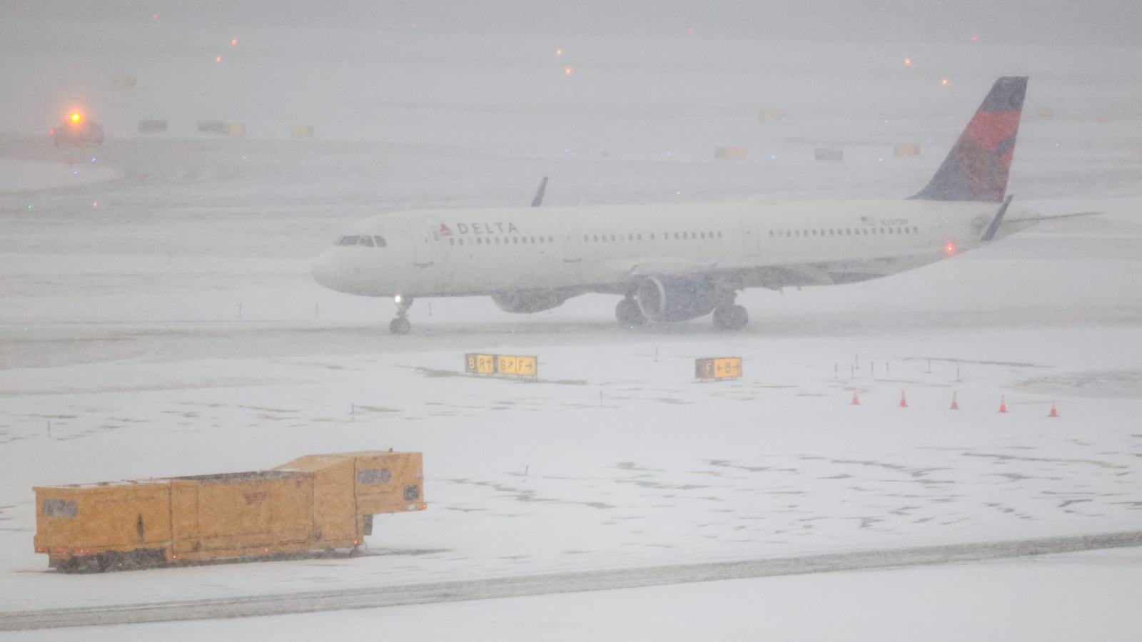 A snow removal machine is seen working while an Airbus A321 Delta Airlines taxied to take off on the tarmac of LaGuardia airport in New York on January 25, 2026. A massive winter storm on January 24, 2026 dumped snow and freezing rain on New Mexico and Texas as it swept across the United States towards the northeast, threatening tens of millions of Americans with blackouts, transportation chaos and bone-chilling cold. Shoppers stripped supermarket shelves as the National Weather Service (NWS) forecast huge snowfall in some areas and possibly "catastrophic" ice accumulations.