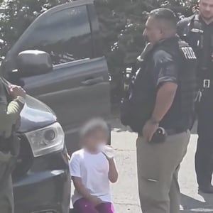 A video still shows a young girl drinking bottled water surrounded by federal immigration agents and local police.