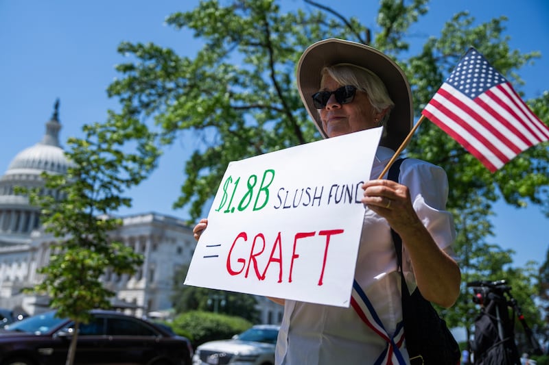 A demonstrator holds a sign referencing the $1.776 billion fund to compensate people who claim they were unfairly targeted by the government, near an event hosted by VoteVets to "call on Congress to do everything in its power to stop Trump's Iran war," outside the U.S. Capitol on Wednesday, May 20, 2026.