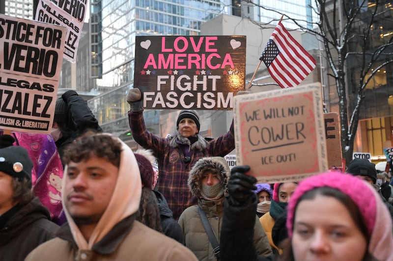 A woman stands elevated in the centre of a crowd holding a sign that says "LOVE AMERICA, FIGHT FASCISM"