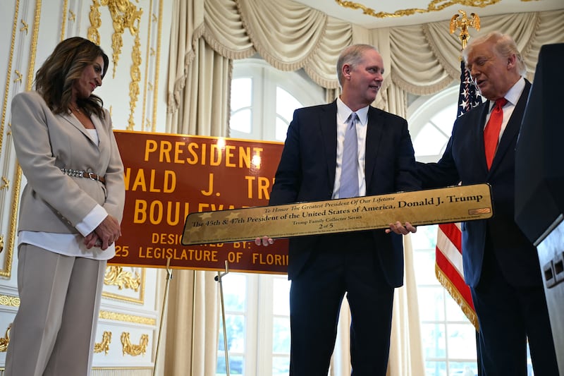 US President Donald Trump (R) is presented with a plaque by the Florida Commissioner of Agriculture Wilton Simpson, as Meg Weinberger (L), a Republican member of the Florida House of Representatives, looks on during a dedication ceremony for Southern Boulevard, in the ballroom at Mar-a-Lago in Palm Beach, Florida, on January 16, 2026. A portion of Palm Beach Southern Boulevard is being renamed as "President Donald J. Trump Boulevard." (Photo by ANDREW CABALLERO-REYNOLDS / AFP via Getty Images)