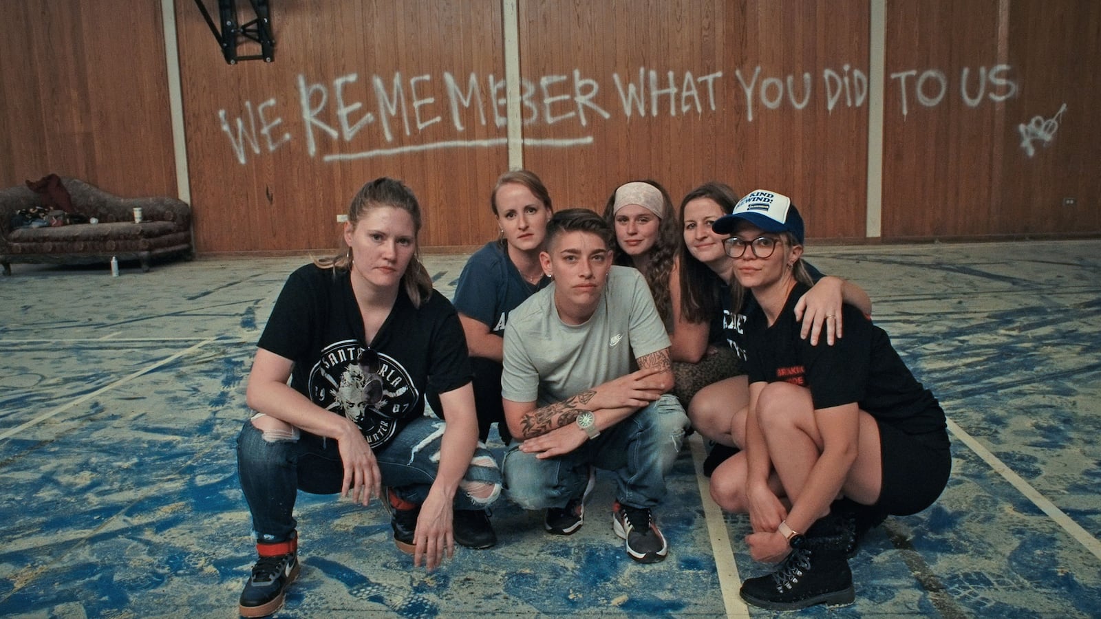 A group of women crowd together to pose for a picture in a room where the phase "we remember what you did to us" is spray painted on the walls
