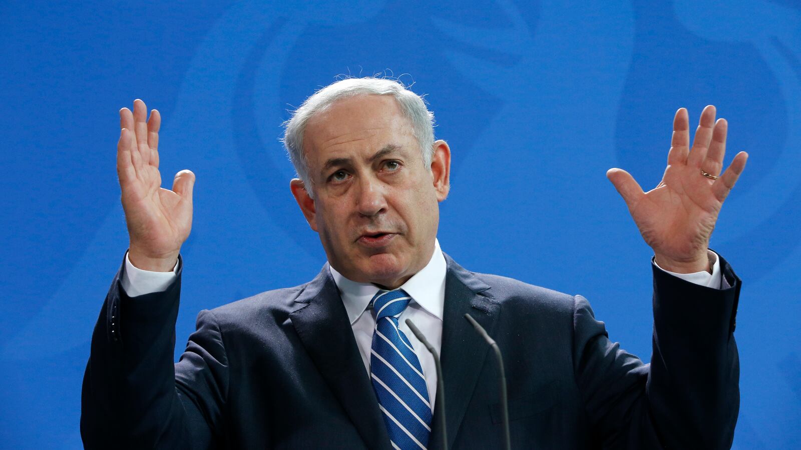 Benjamin Netanyahu speaks on stage with his hands raised.