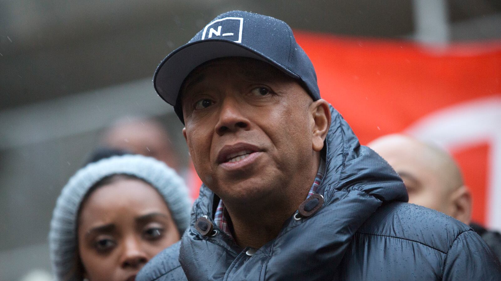 Russell Simmons, wearing a hat, prepares to speak at an outside event.