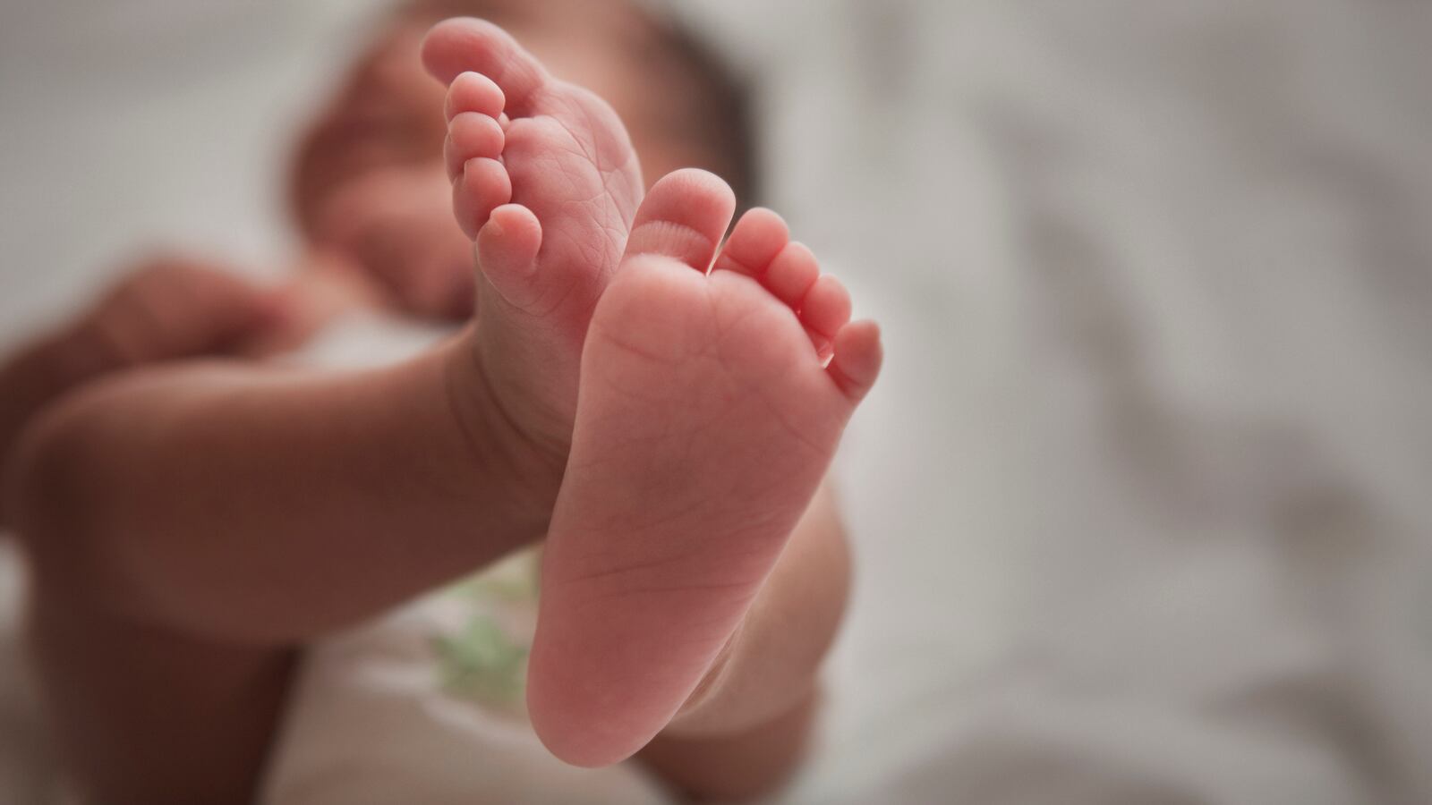 A newborn baby lying down with her feet in the air.