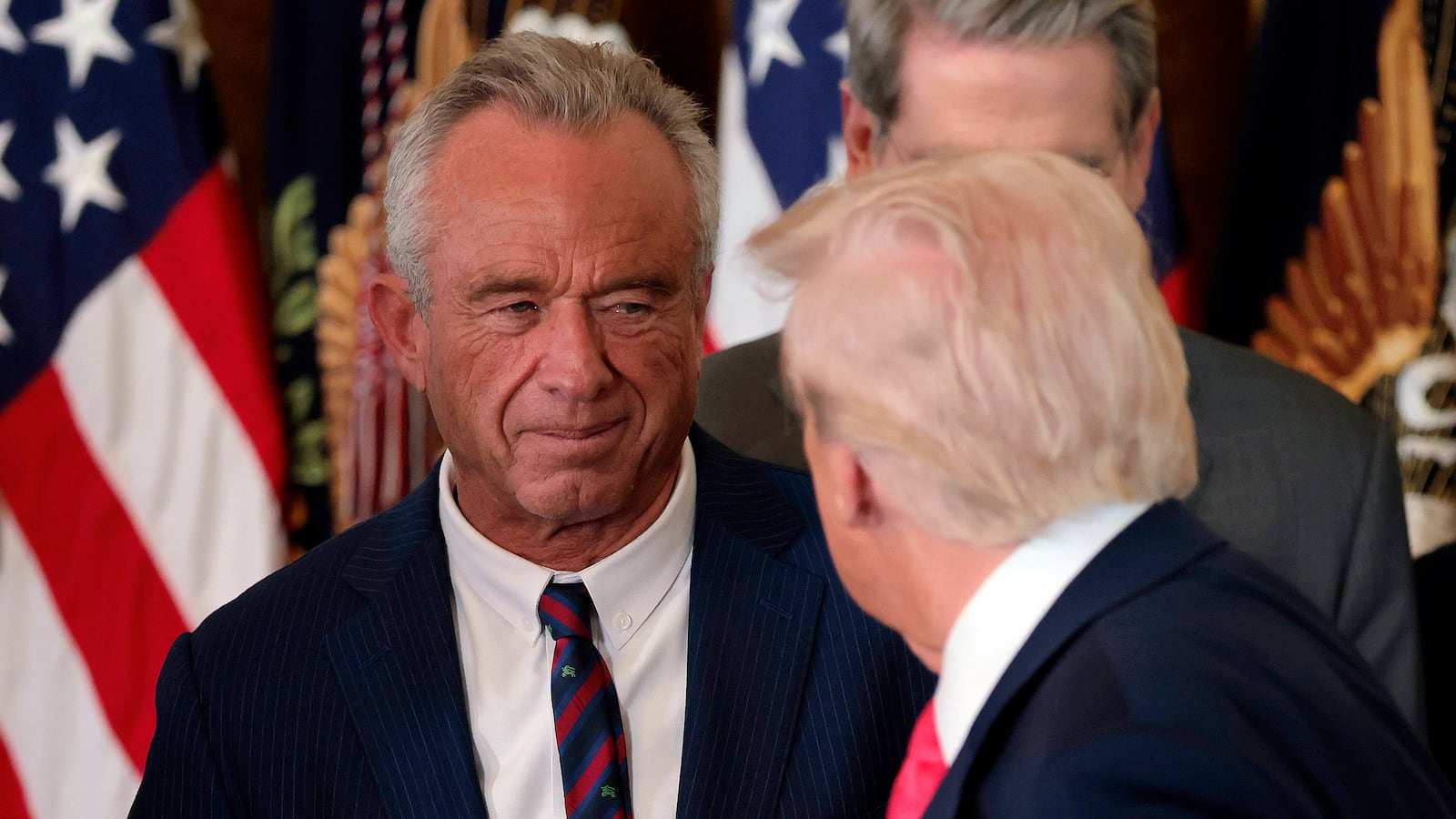 WASHINGTON, DC - NOVEMBER 13: President Donald Trump, shakes hands with Health and Human Services Secretary Robert F. Kennedy Jr. alongside Secretary of Housing and Urban Development Scott Turner (L) after Trump signed the "Fostering the Future" executive order the East Room of the White House on November 13, 2025 in Washington, DC. The executive order, championed by first lady Melania Trump, works to expand opportunities for education, career development, housing and other resources for youth transitioning from foster care to adulthood. (Photo by Heather Diehl/Getty Images)