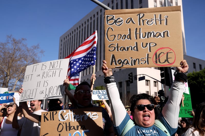 Prostestors stand holding signs and an upside down American flag