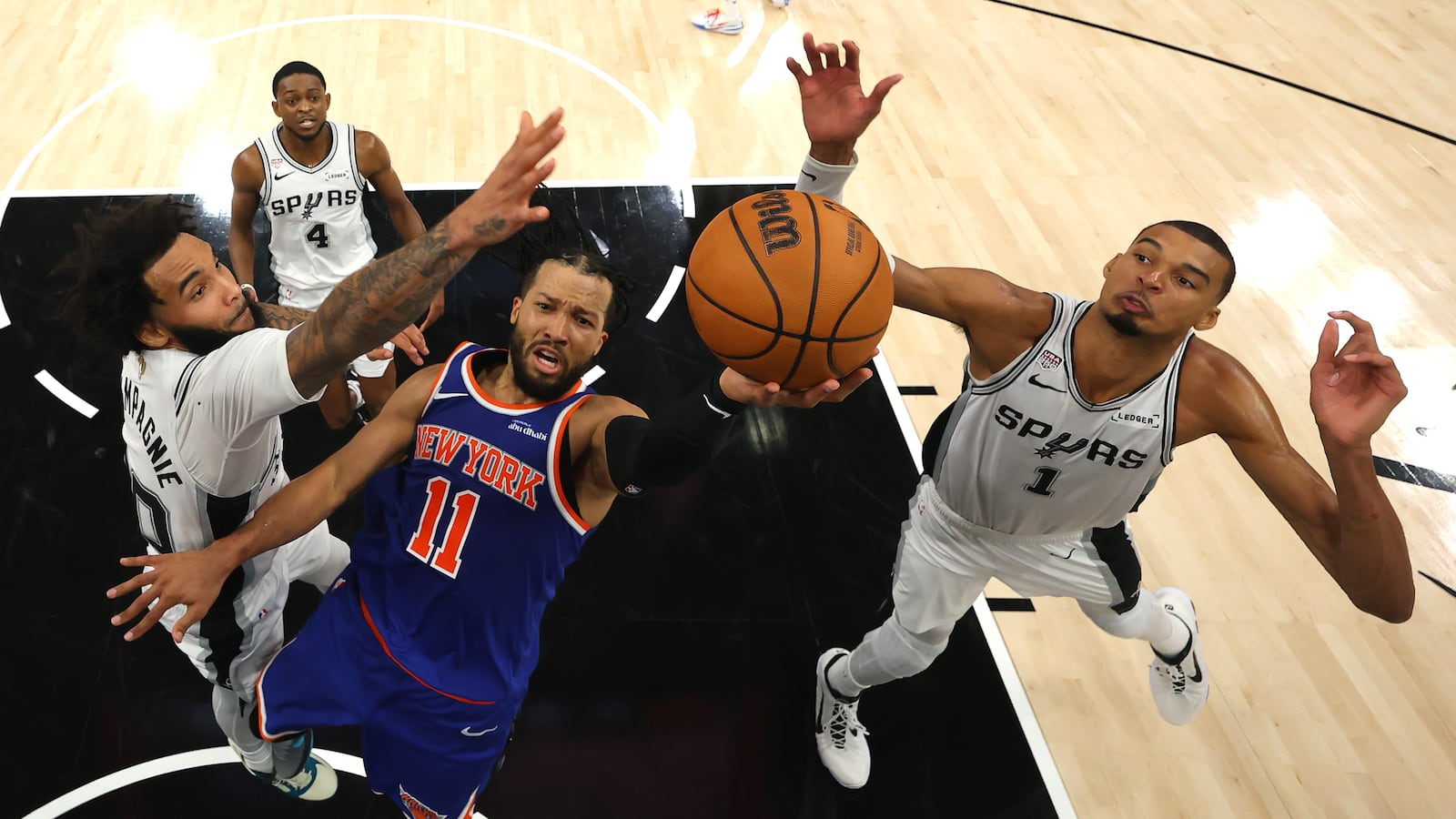 Jalen Brunson of the New York Knicks shoots the ball between Julian Champagnie and Victor Wembanyama