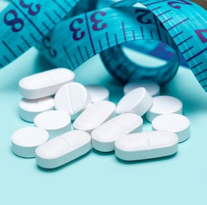 GLP-1 drugs spilling out of pill bottle and measuring tape on blue background