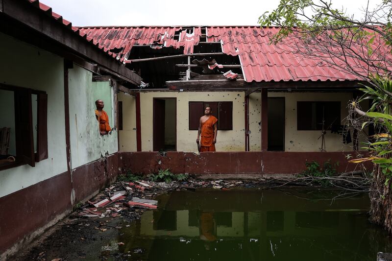Monks stand near a damaged dorm at Thai Niyom temple, which was hit by Cambodian artillery