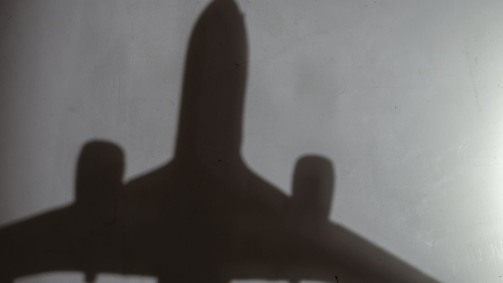 Dark silhouette of an airplane on a light gray wall.