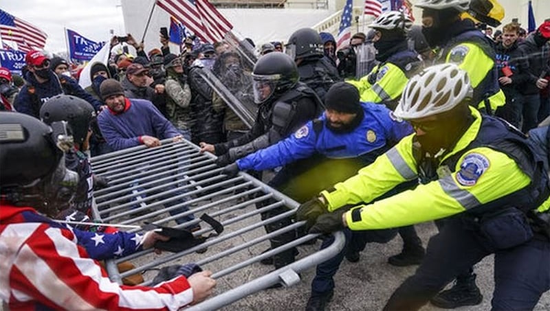 Christopher Quaglin, far left, wearing USA flag jacket, pulling a bike rack from police officers outside the U.S. Capitol on Jan. 6, 2021.